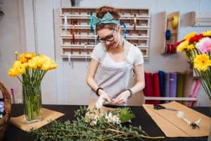 Smiling attractive young woman florist in glasses standing and making bouquet in flower shop